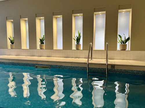 Piscine couverte turquoise, niches lumineuses et plantes vertes