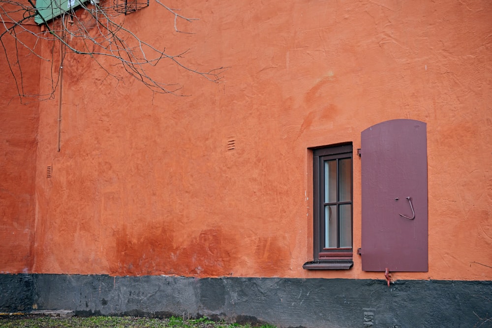 ein orangefarbenes Gebäude mit einem Fenster und einem lila Fensterladen