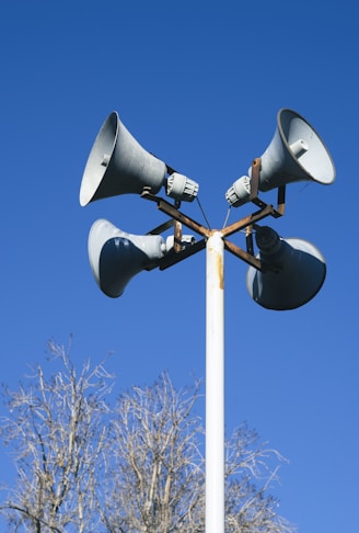 a loudspeaker on top of a white post with a bright blue sky background