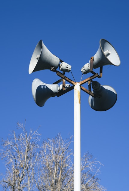 a loudspeaker on top of a white post with a bright blue sky background