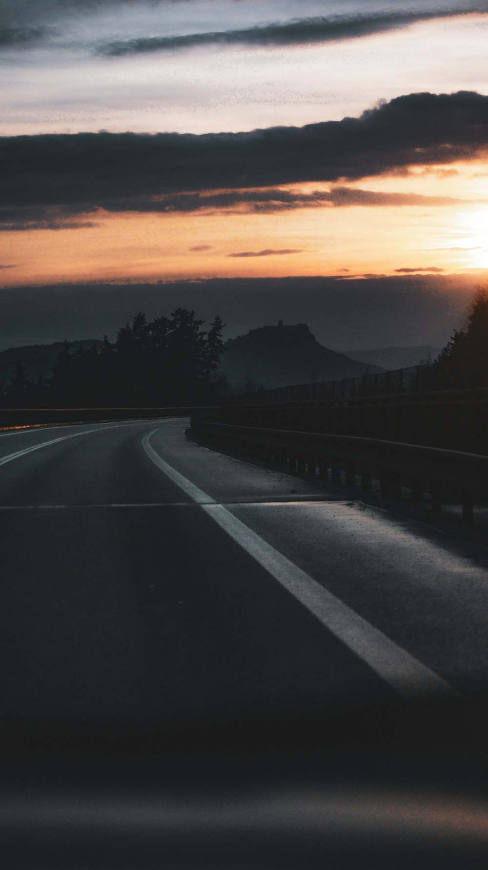 the sun is setting over the mountains on the highway