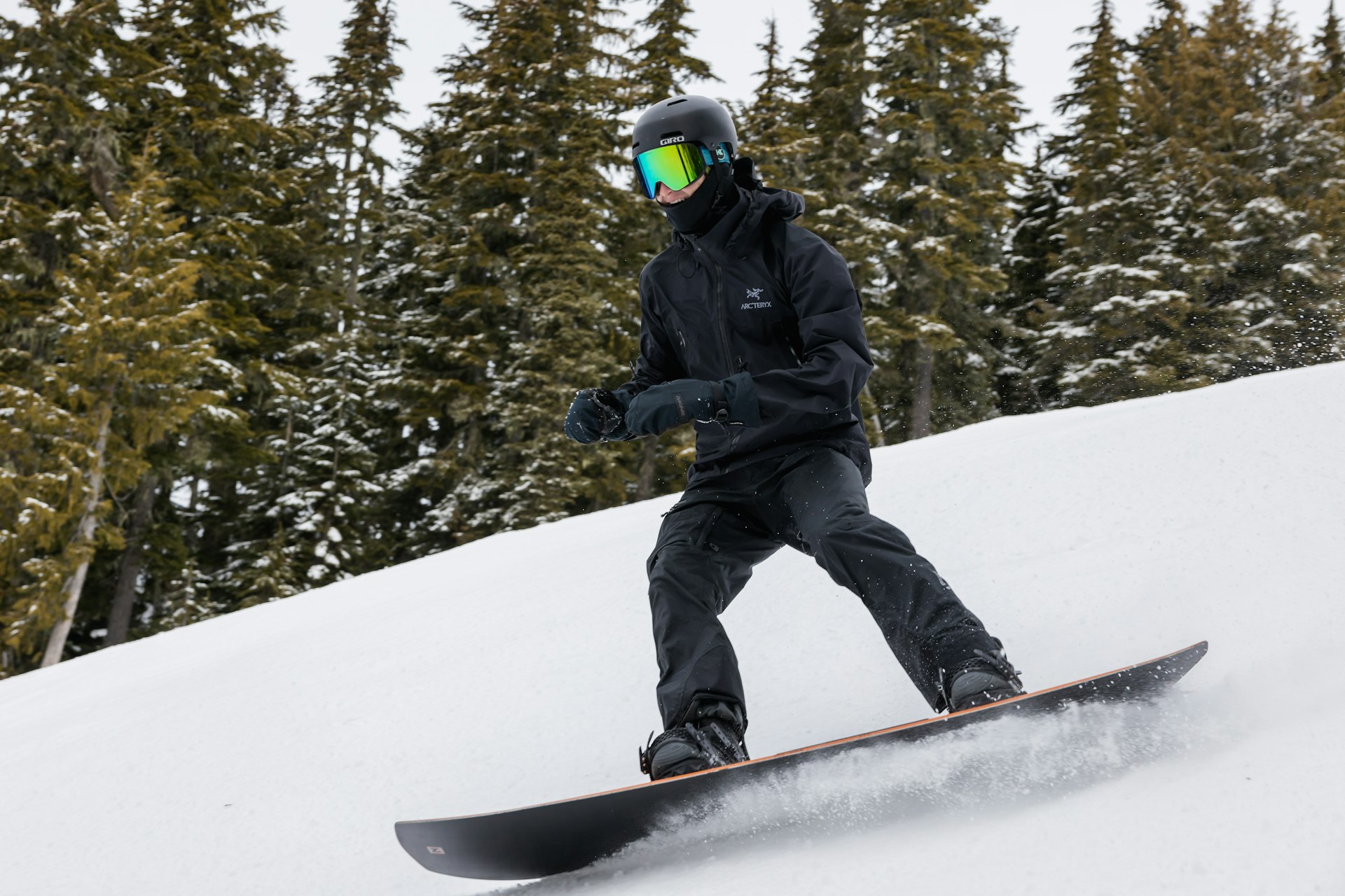 Male snowboarder in black gear cruising down a tree-lined groomer