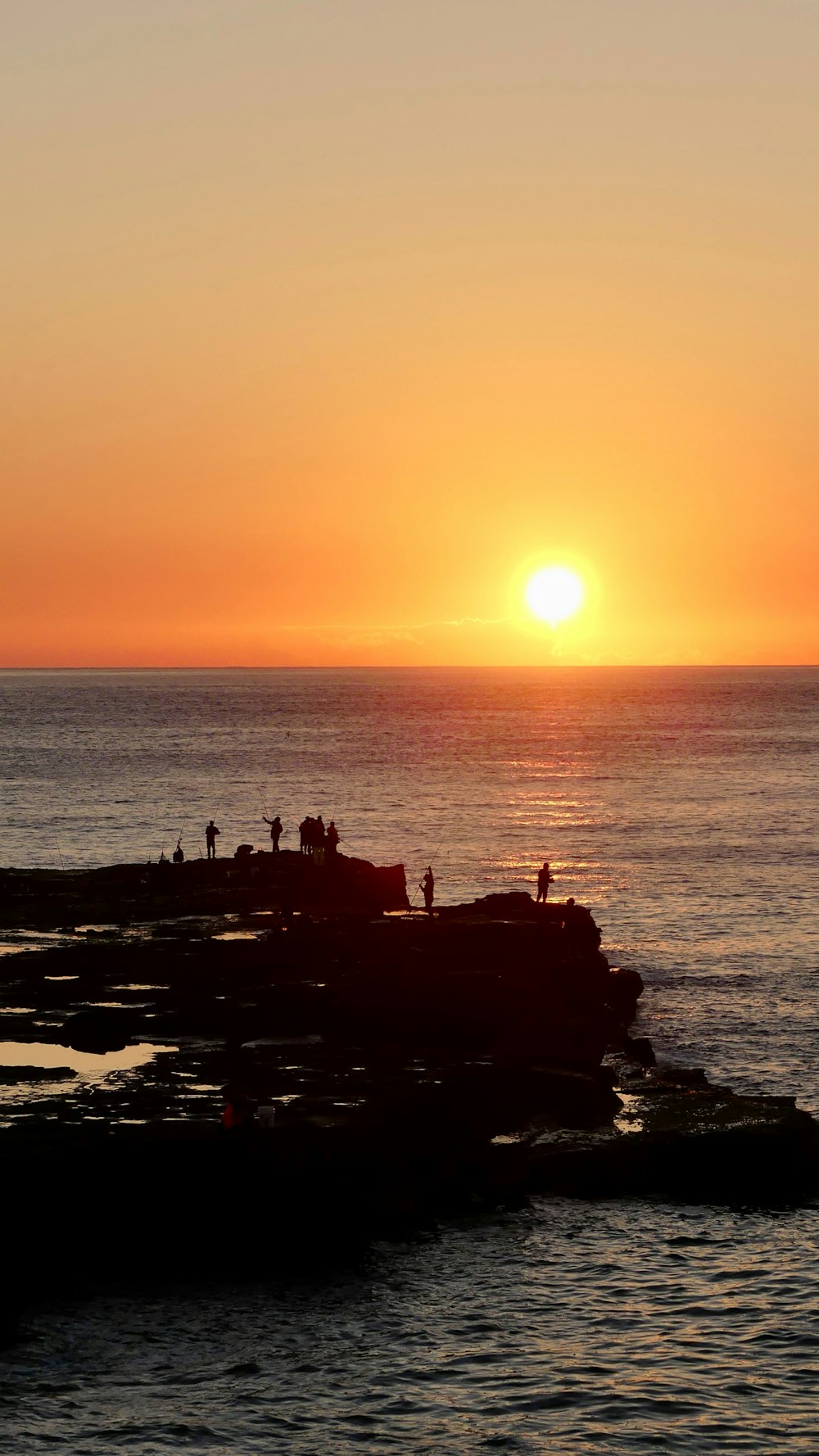 the sun is setting over the ocean with people on the rocks