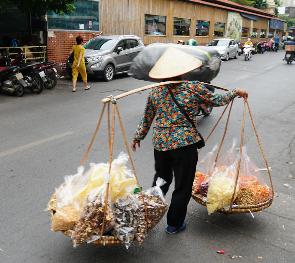 a woman carrying two baskets of food down a street