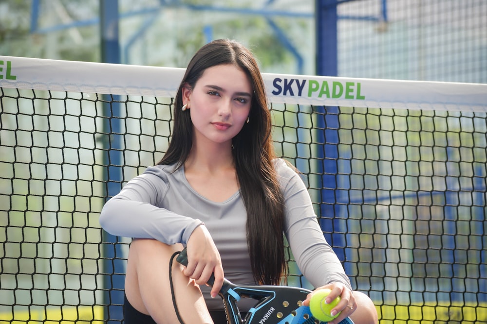 a woman sitting on a tennis court holding a racquet