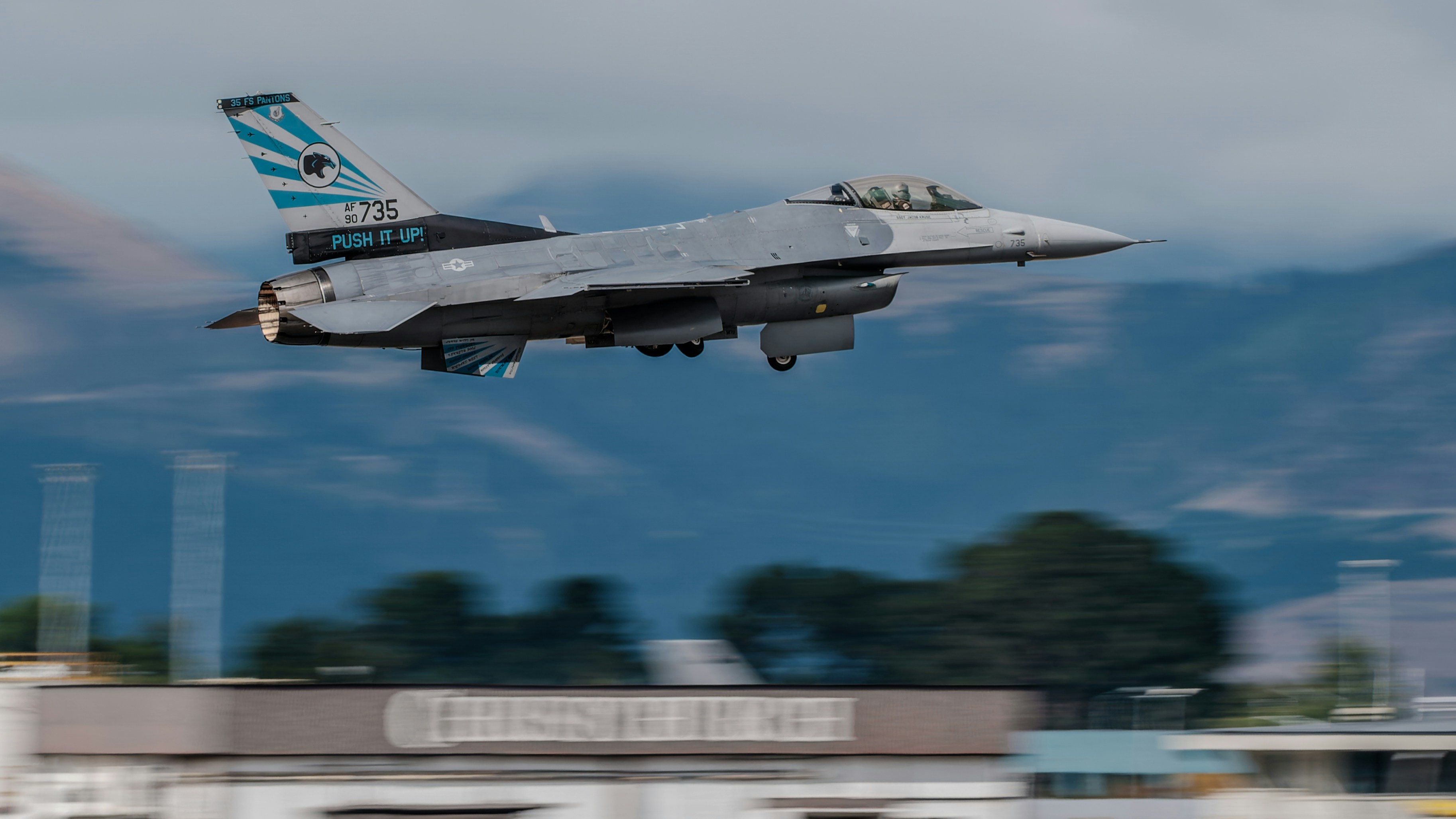 a fighter jet flying through the air with mountains in the background