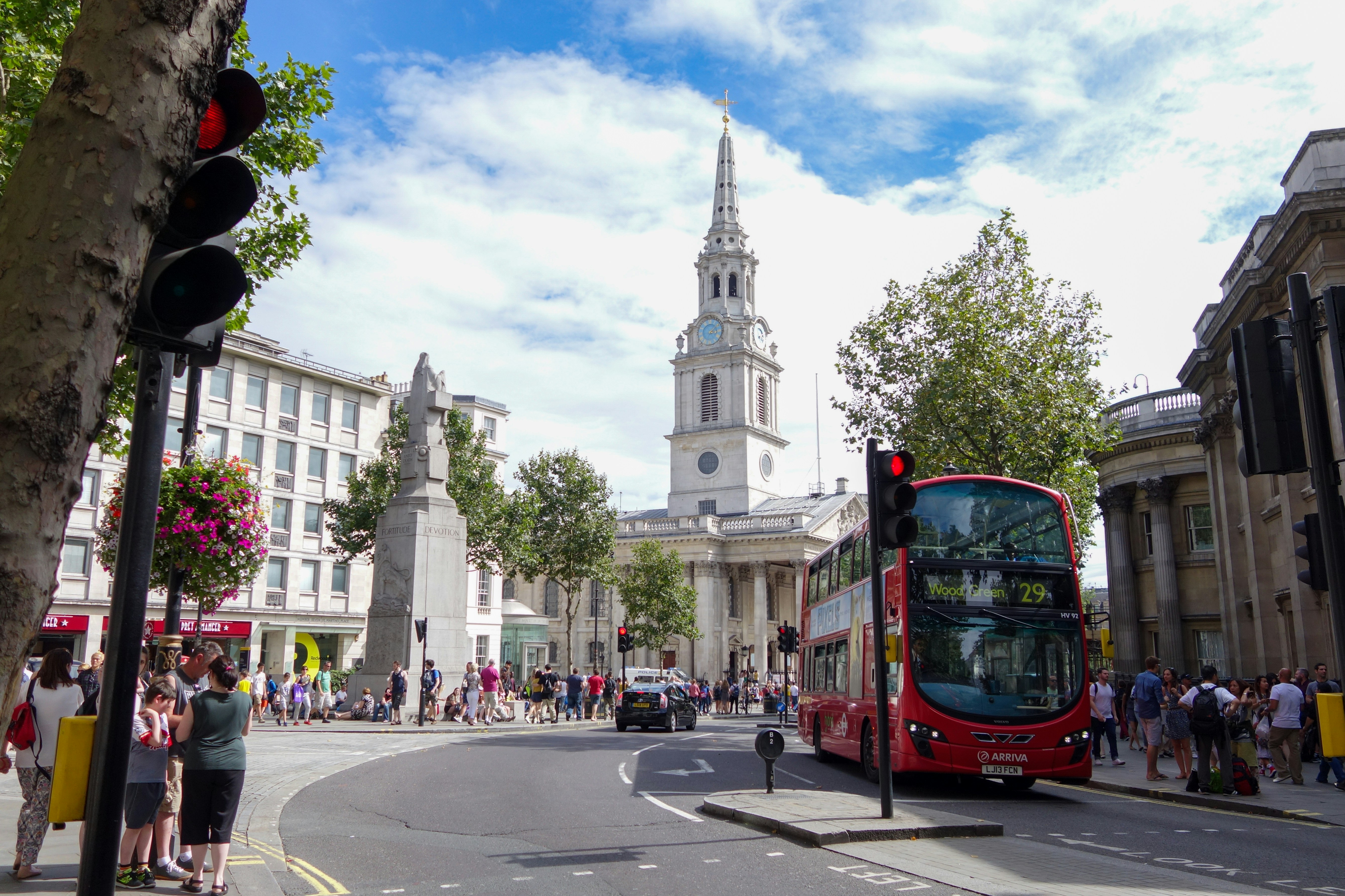 In the heart of London, the red double-decker bus, a city emblem, traverses the junction. Historic architecture and a bustling crowd frame this quintessential urban snapshot, under the watchful gaze of an iconic church spire.