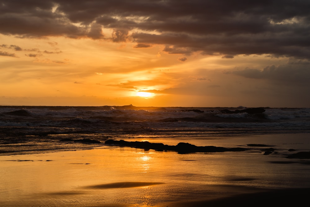 the sun is setting over the ocean on a cloudy day