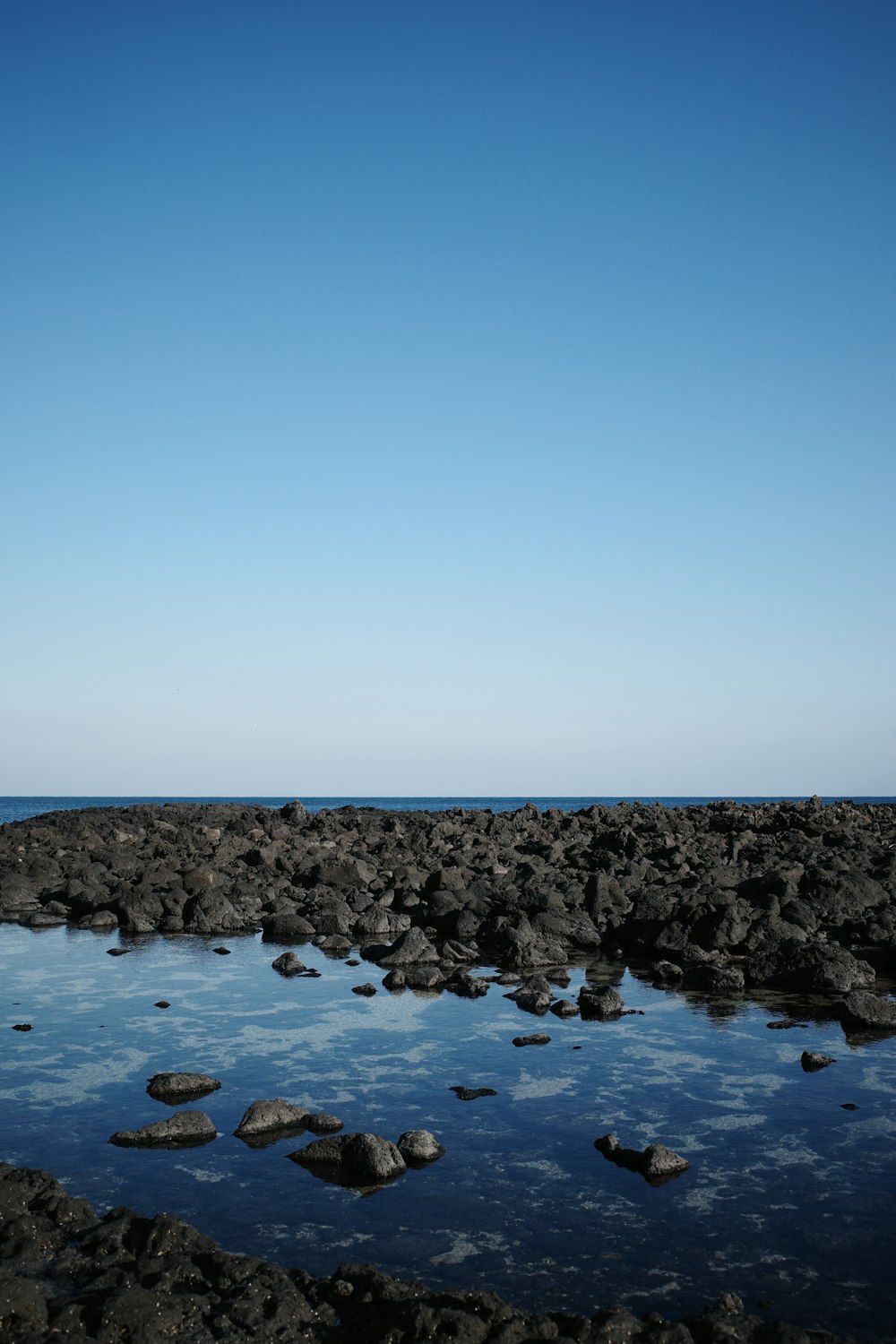 a body of water surrounded by rocks under a blue sky