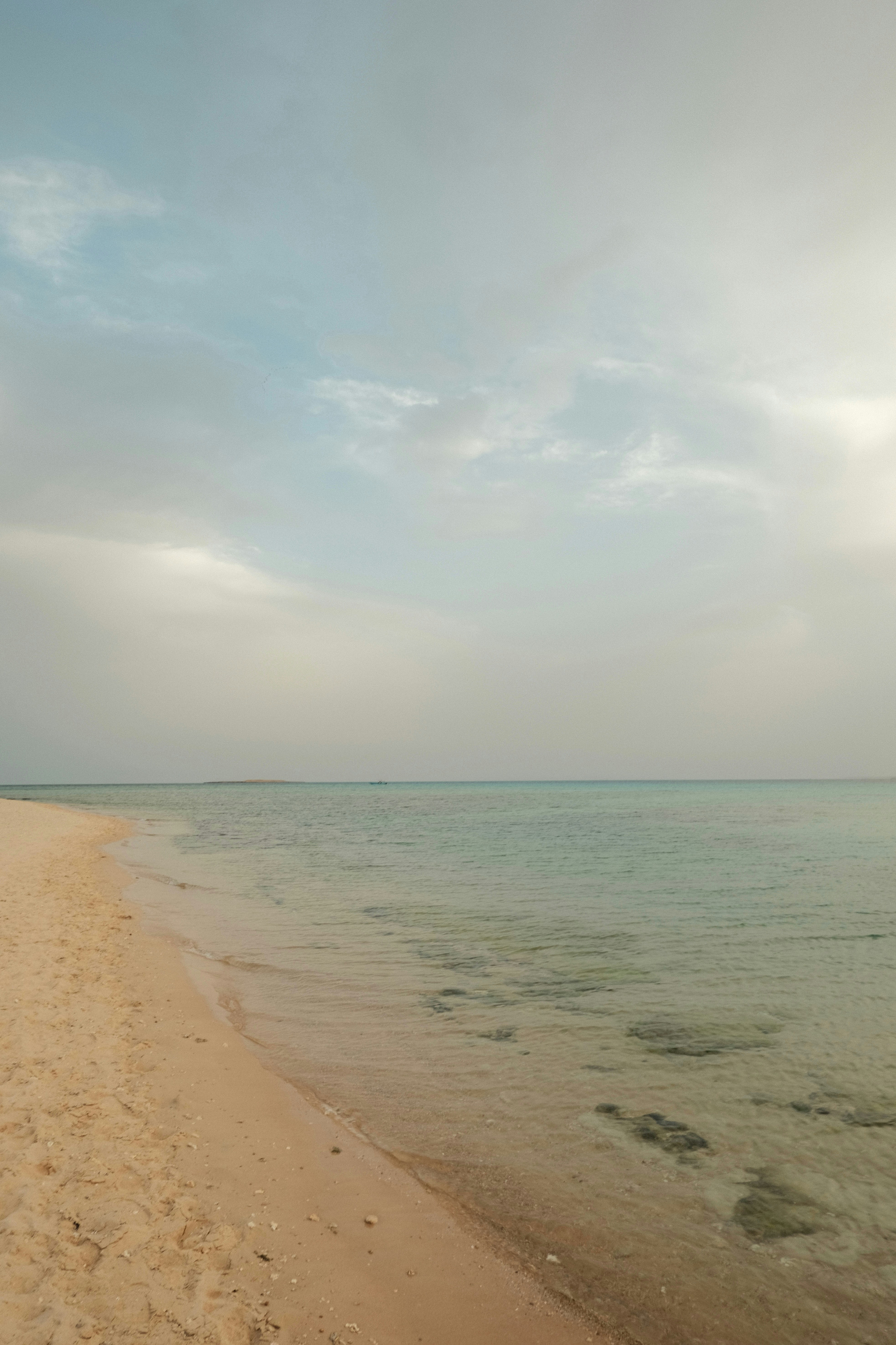 a sandy beach next to the ocean under a cloudy sky