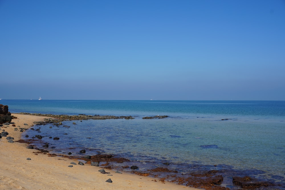 a sandy beach with blue water and a boat in the distance