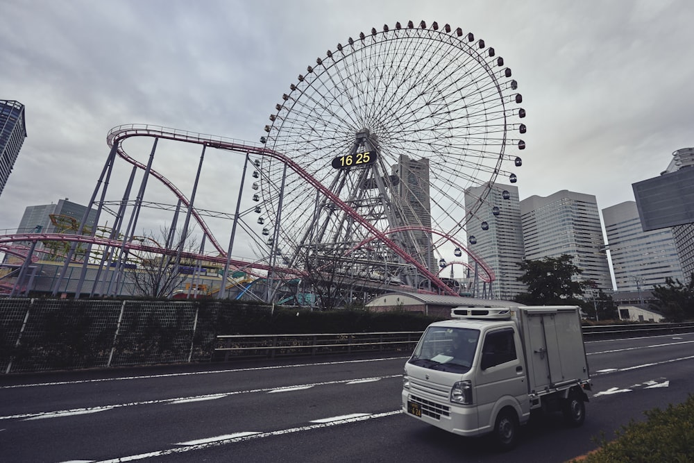 a white truck driving down a street next to a ferris wheel