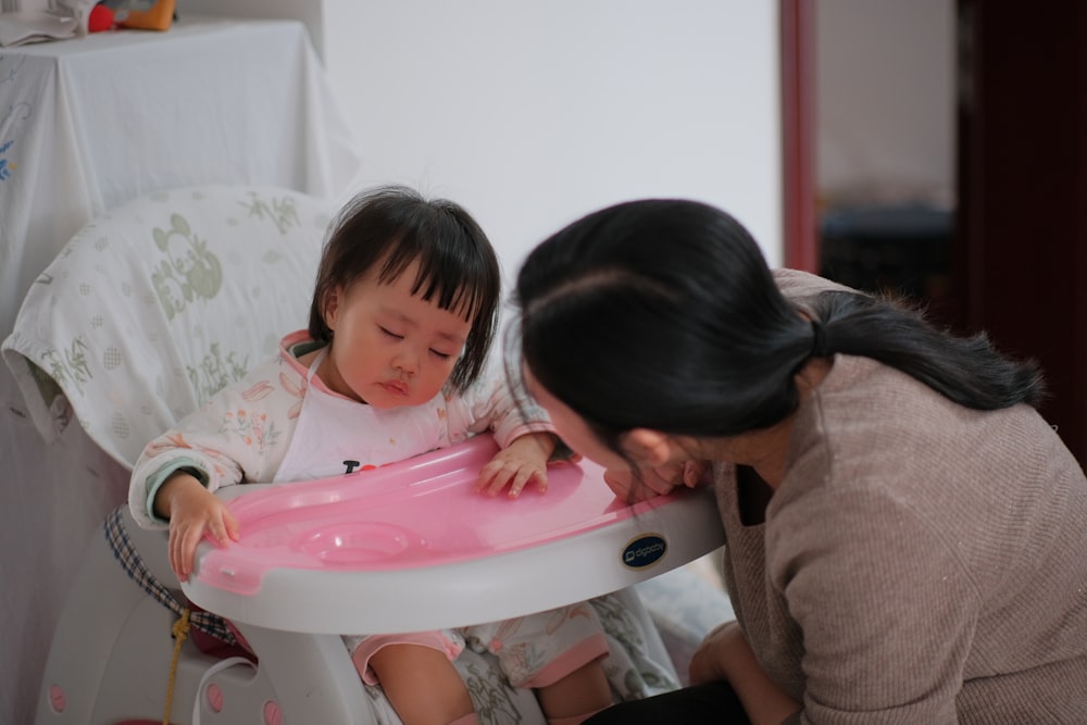a woman kneeling down next to a baby in a high chair