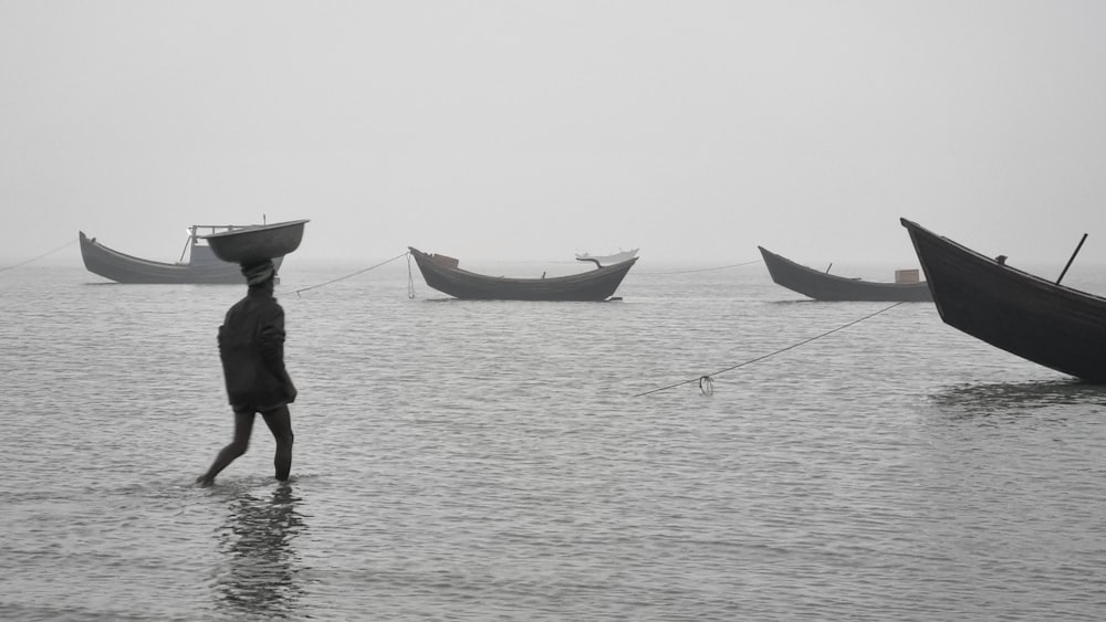 a person walking in the water with three boats in the background