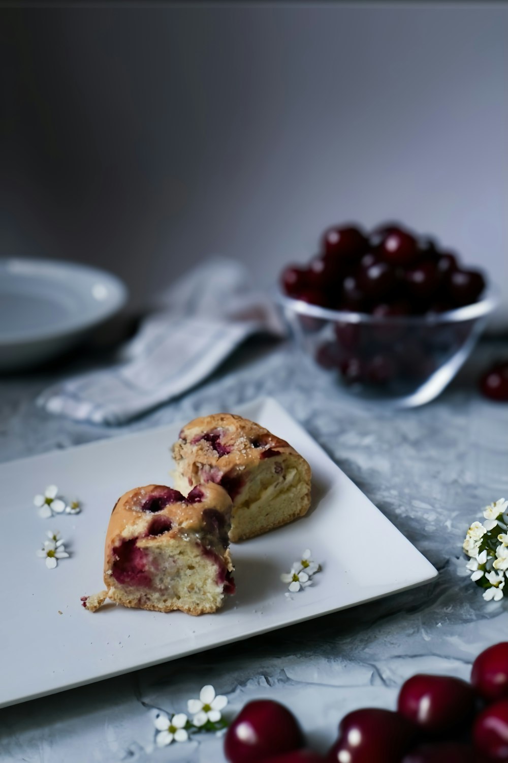 a white plate topped with a piece of cake next to a bowl of cherries
