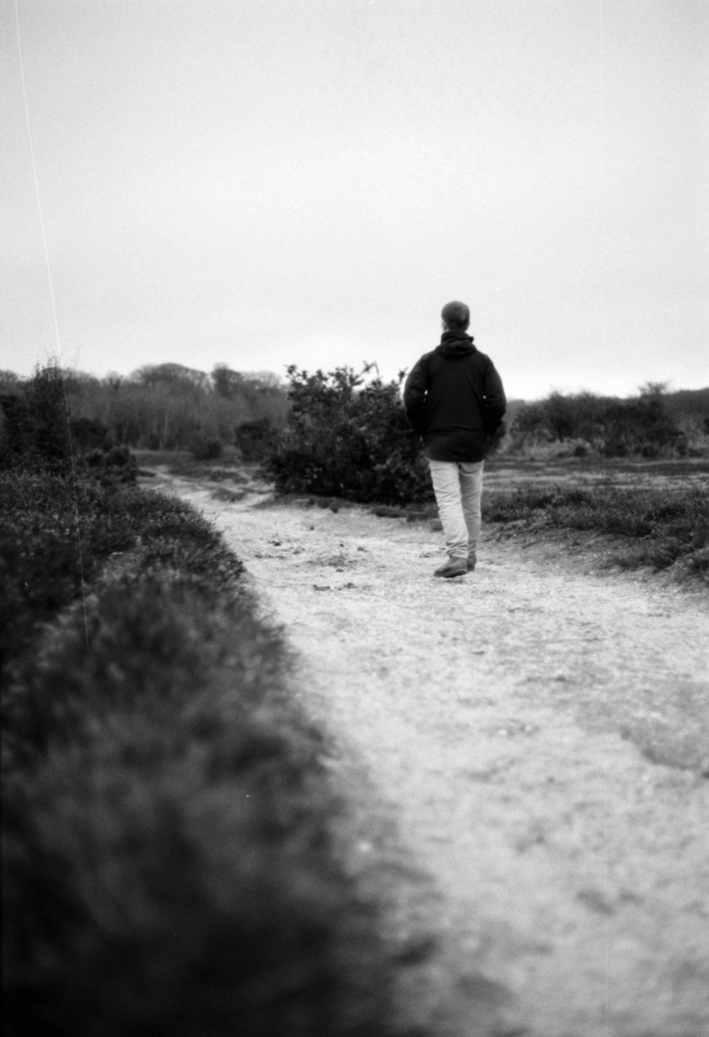 a man walking down a dirt road in a black and white photo