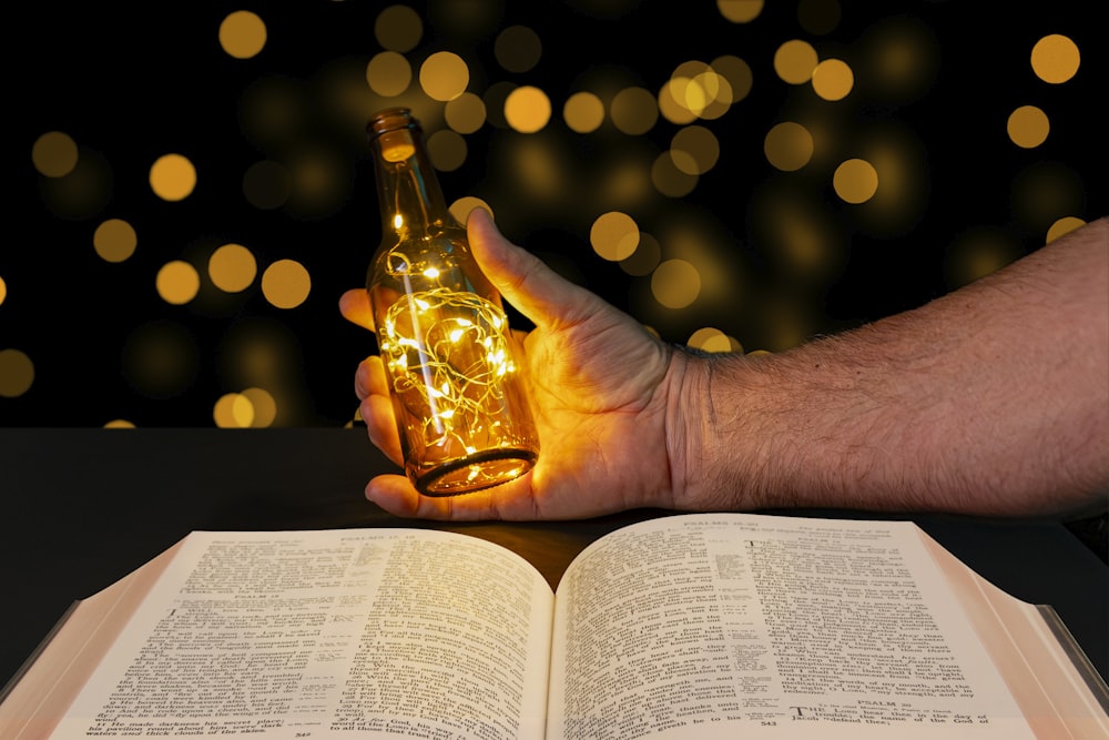 a man holding a bottle of beer over an open book