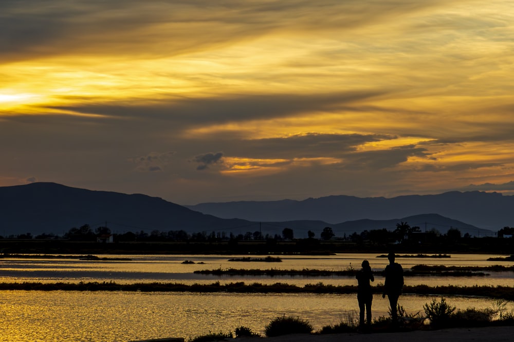 a couple of people standing on top of a beach next to a body of water