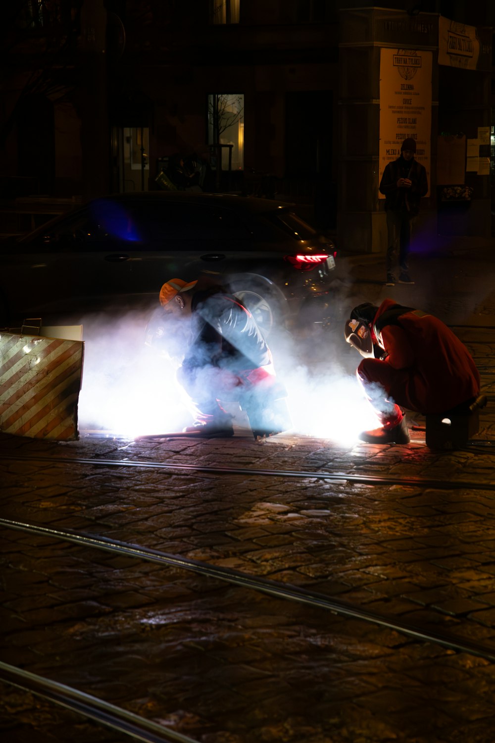 two men working on a car on a city street