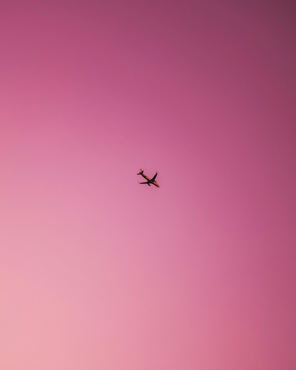 an airplane is flying in the pink sky