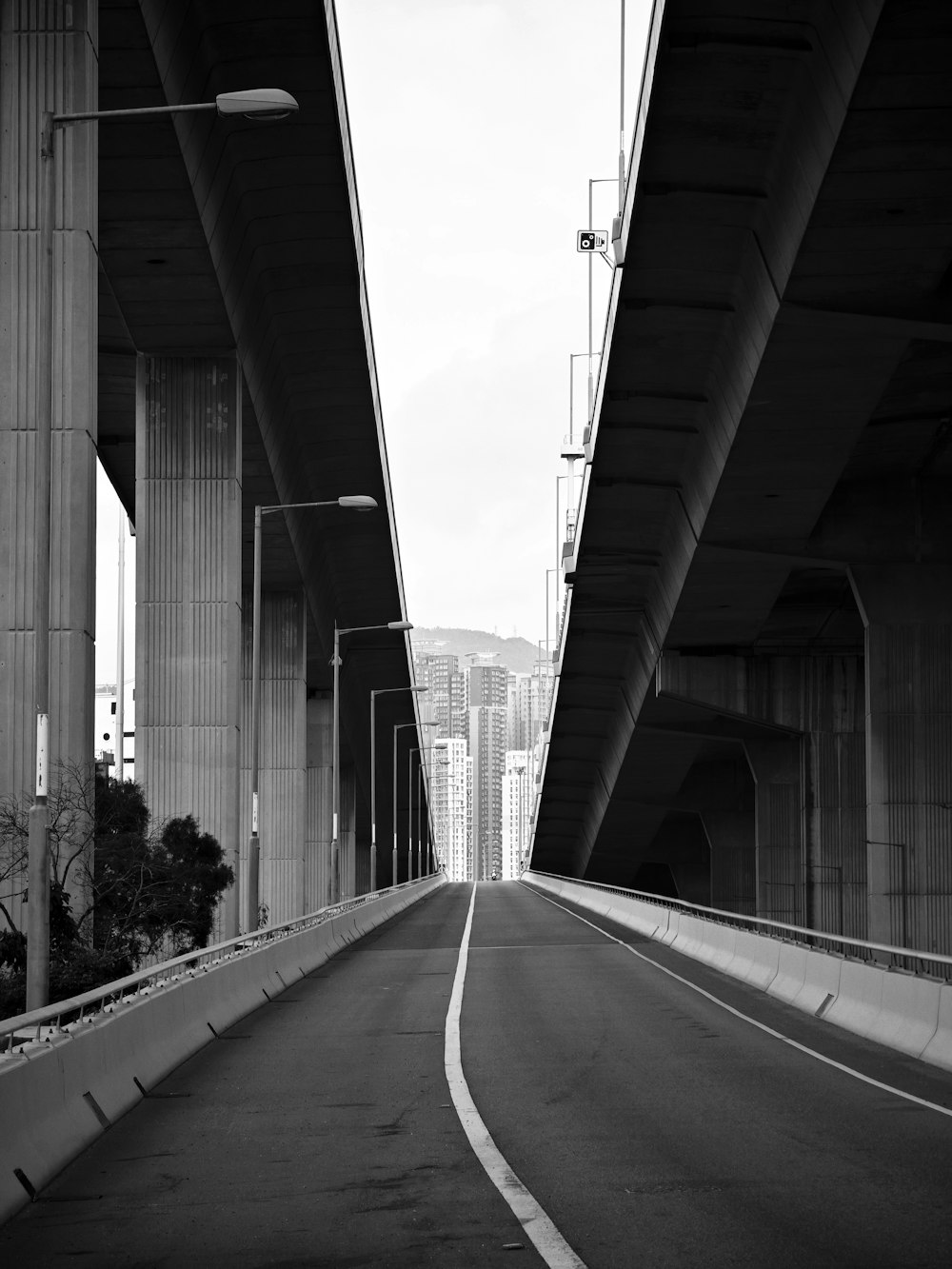a black and white photo of a highway going under a bridge