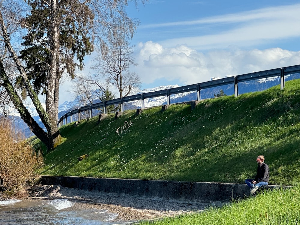 a man sitting on a hill next to a river