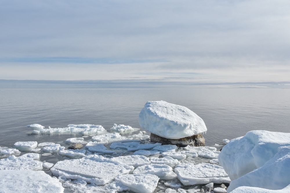 a rock covered in snow next to a body of water