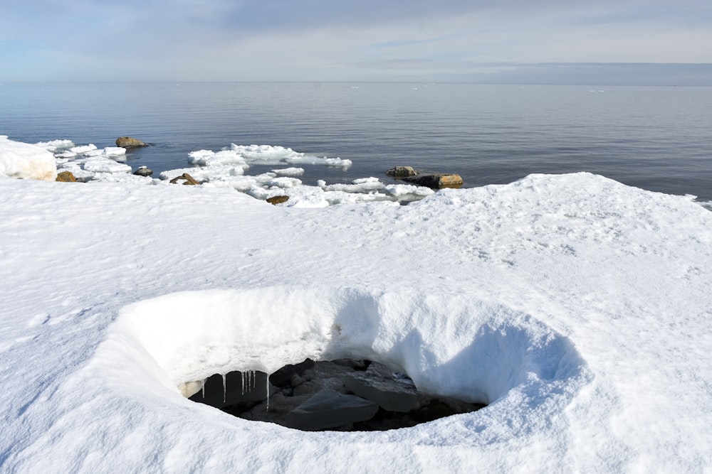 a hole in the snow with a body of water in the background