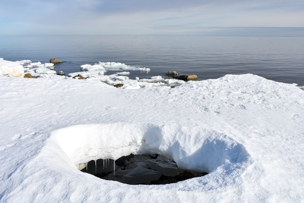 ein Loch im Schnee mit einem Gewässer im Hintergrund