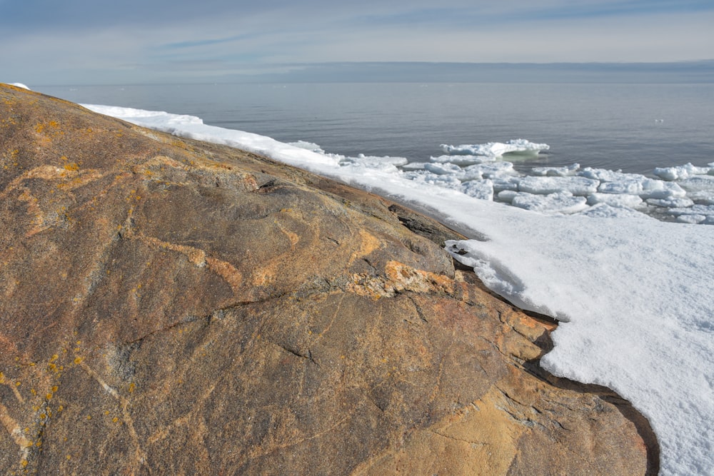 a large rock covered in snow next to a body of water