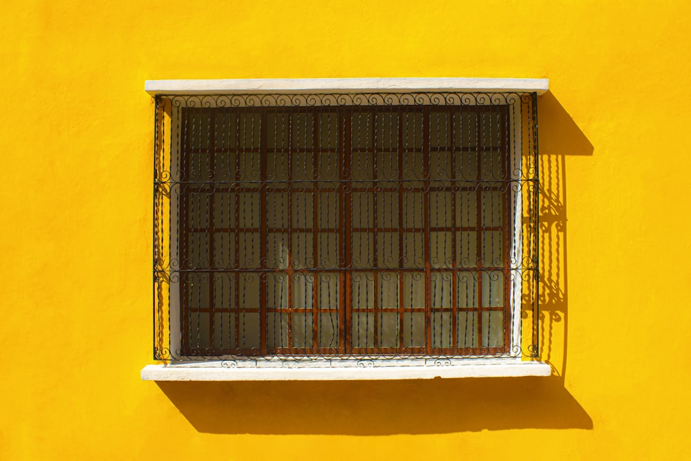 a yellow wall with a window with bars on it