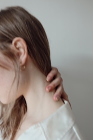 a woman in a white shirt is holding her neck