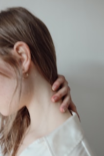a woman in a white shirt is holding her neck