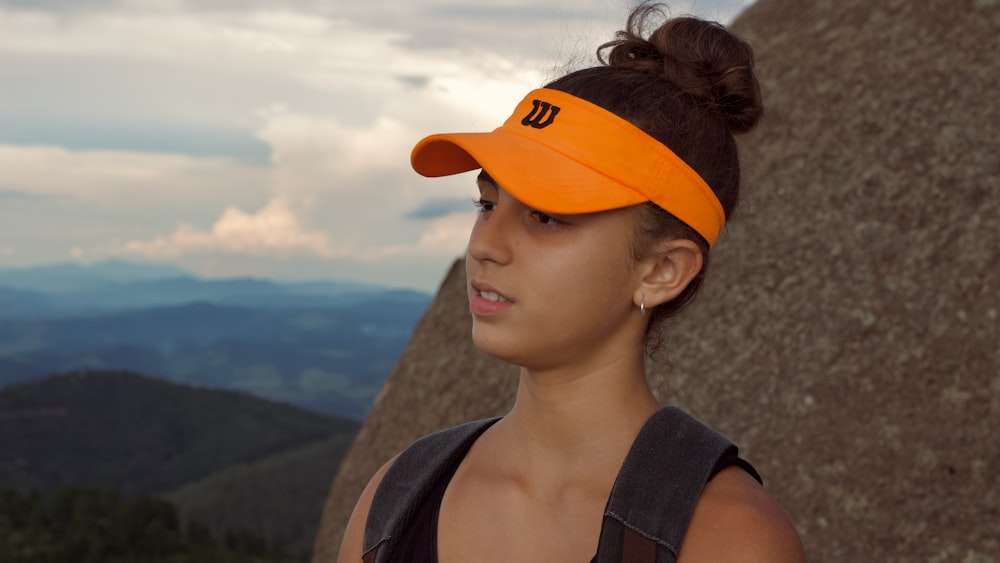 a woman wearing an orange visor on top of a mountain