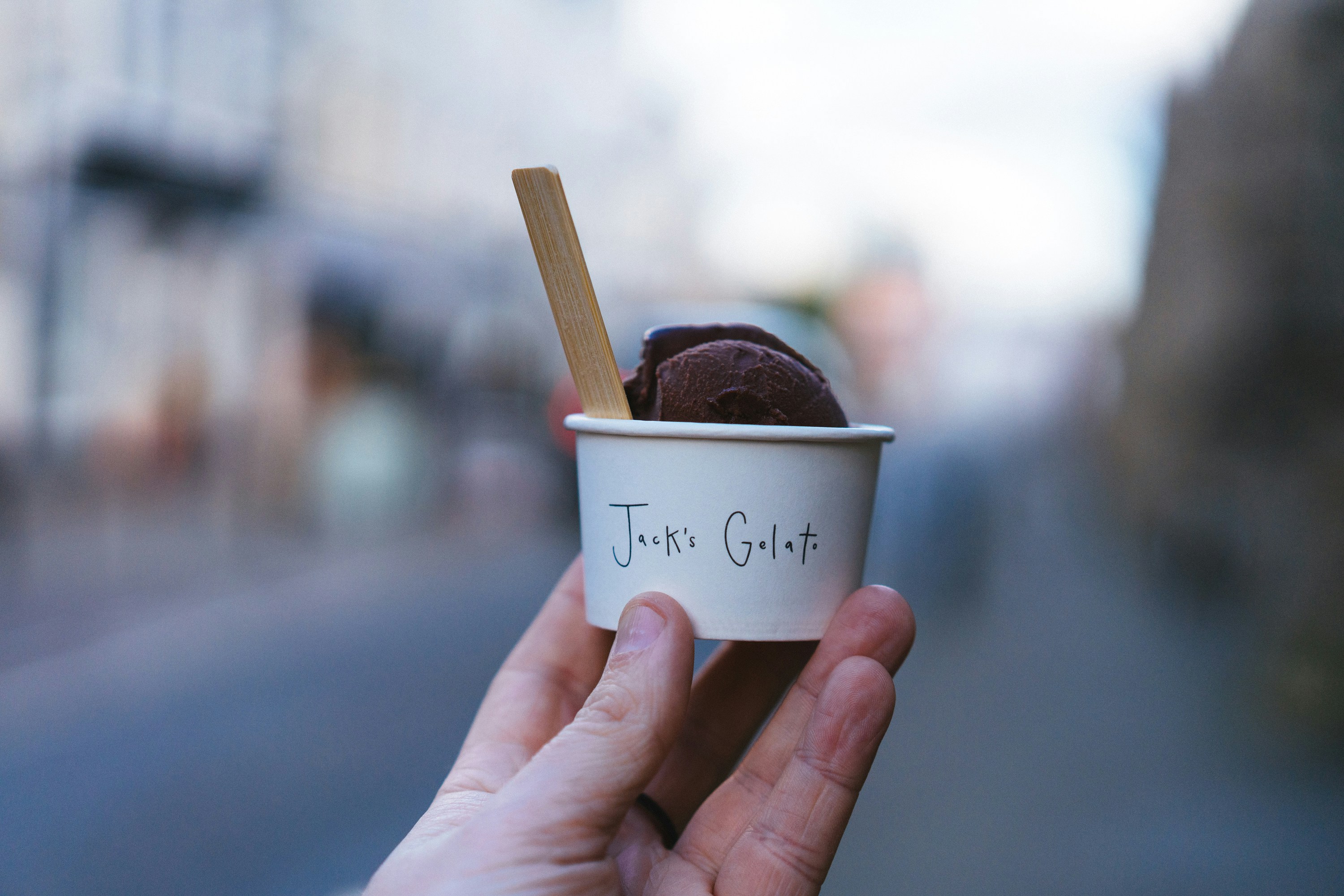 a hand holding a cup of ice cream with a stick in it