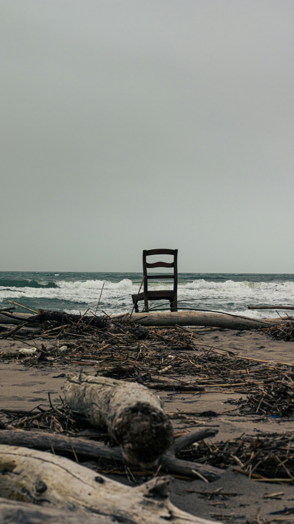 a wooden chair sitting on top of a beach next to the ocean