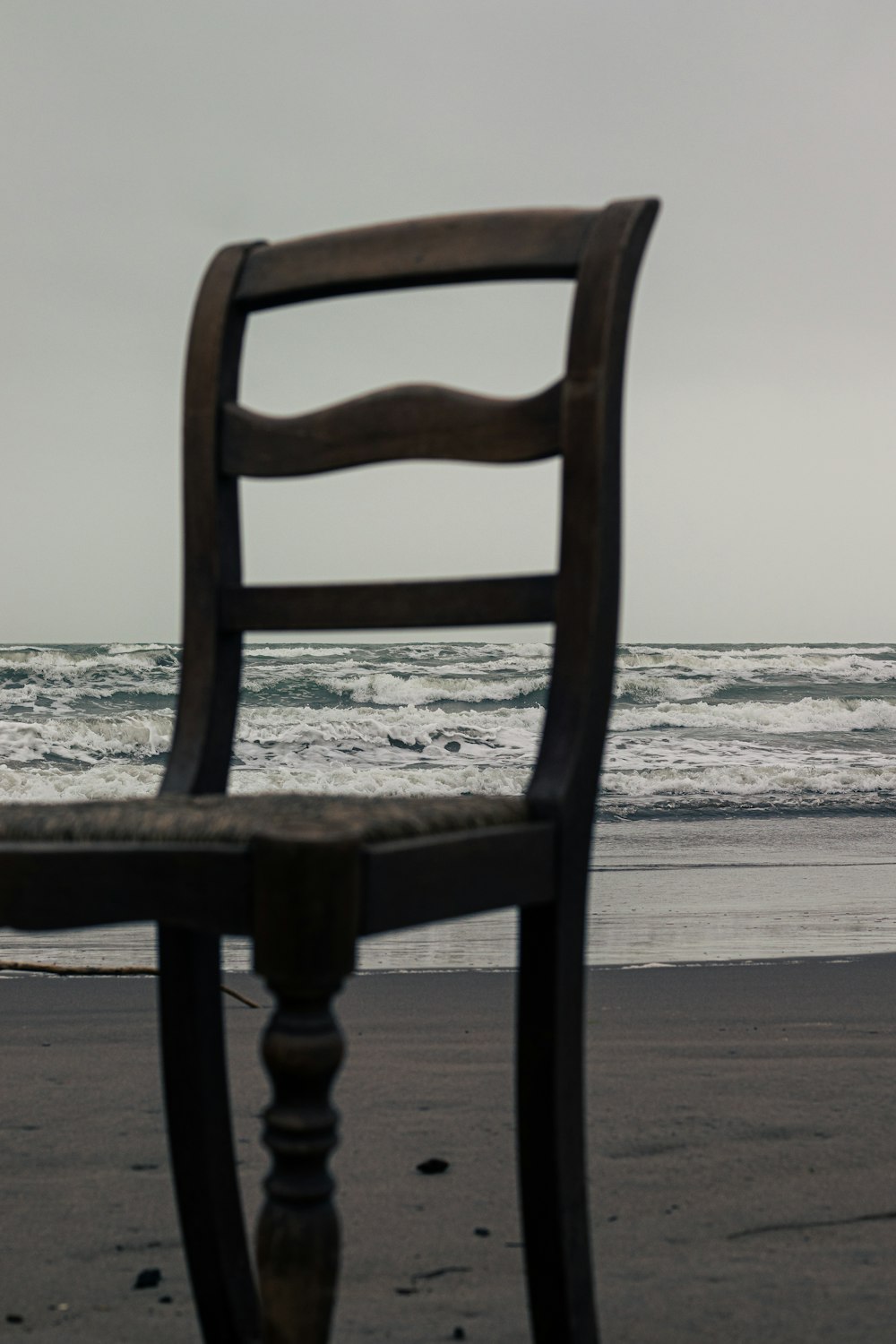 a wooden chair sitting on top of a beach next to the ocean