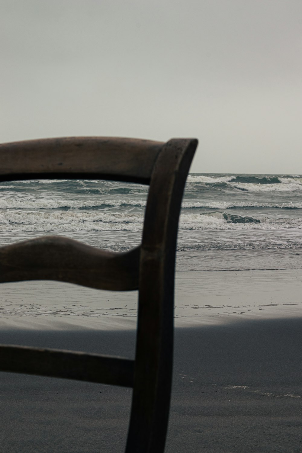 a wooden chair sitting on top of a beach next to the ocean