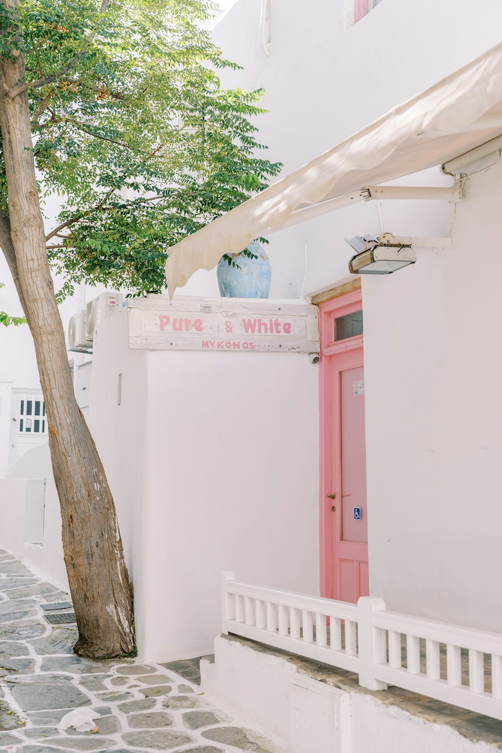 a white building with a pink door and a tree