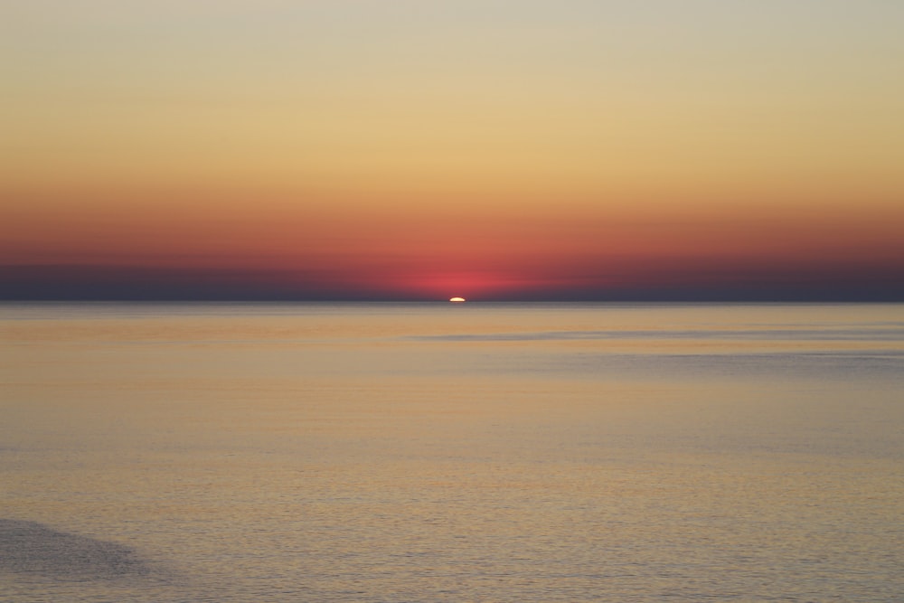 the sun is setting over the ocean with a boat in the water