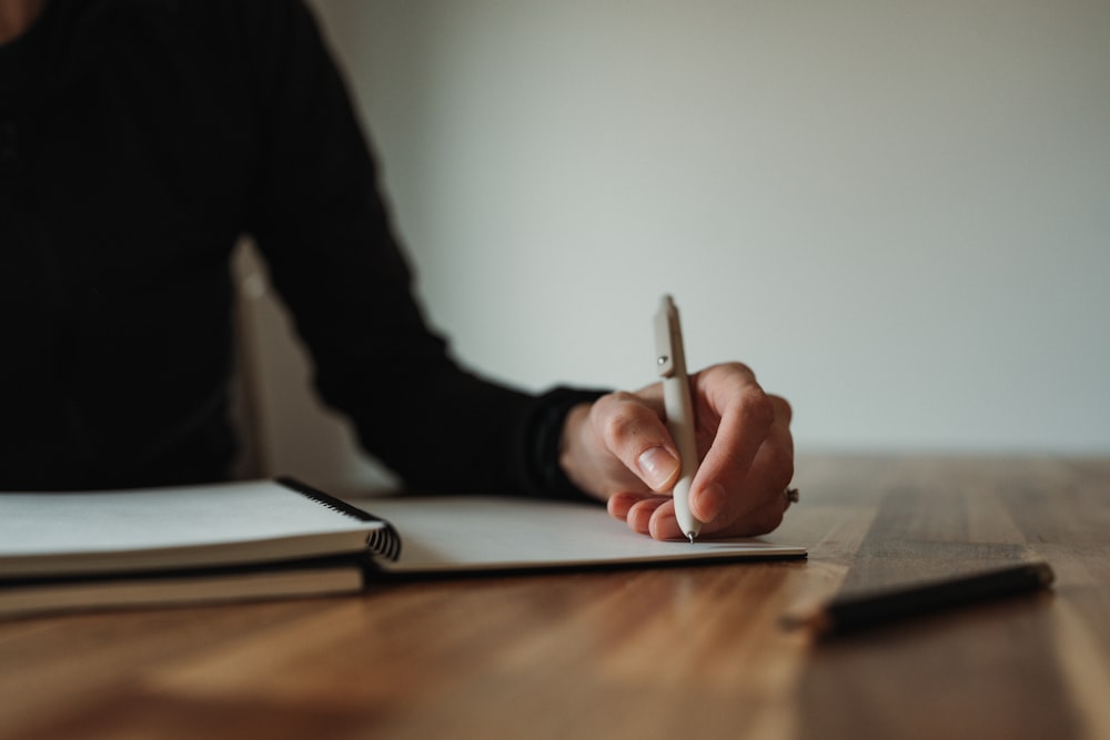 una persona sentada en una mesa escribiendo en una hoja de papel