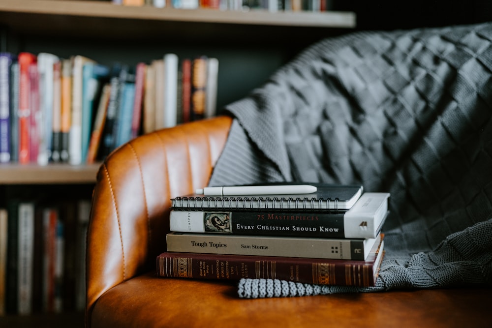 a stack of books sitting on top of a brown chair