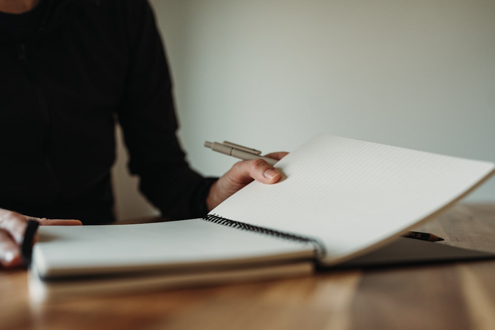 a person holding a pen and writing on a notebook