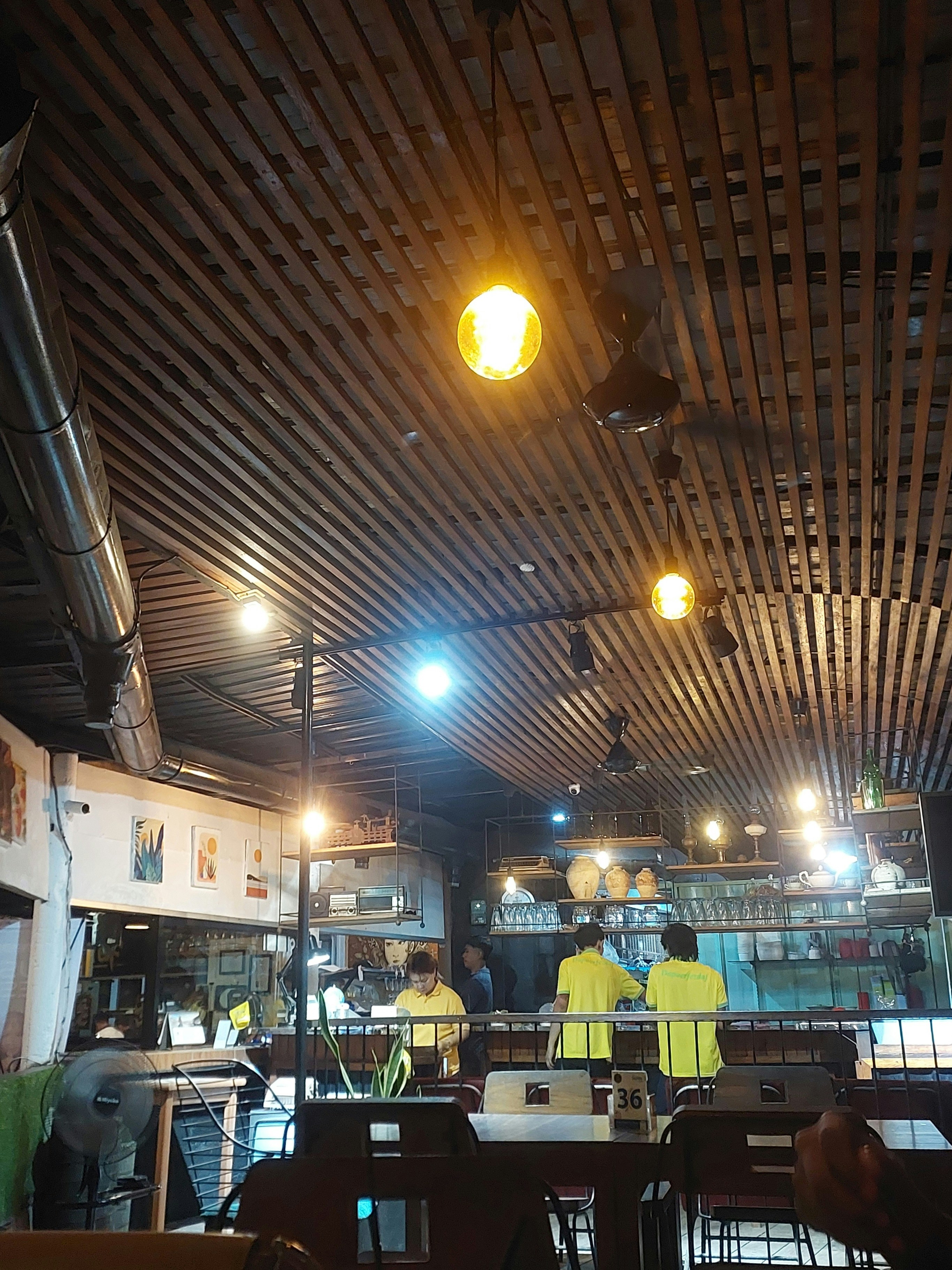 Interior restaurant cu lumini calde galbene, mese de lemn cu lumânări, pereți cărămidă, atmosferă intimă și romantică, clienți în fundal, seară