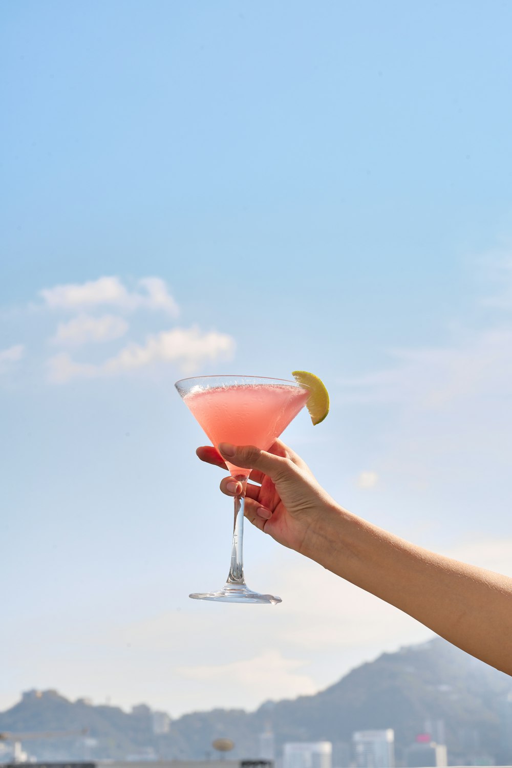 a hand holding a martini glass with a lemon wedge in it