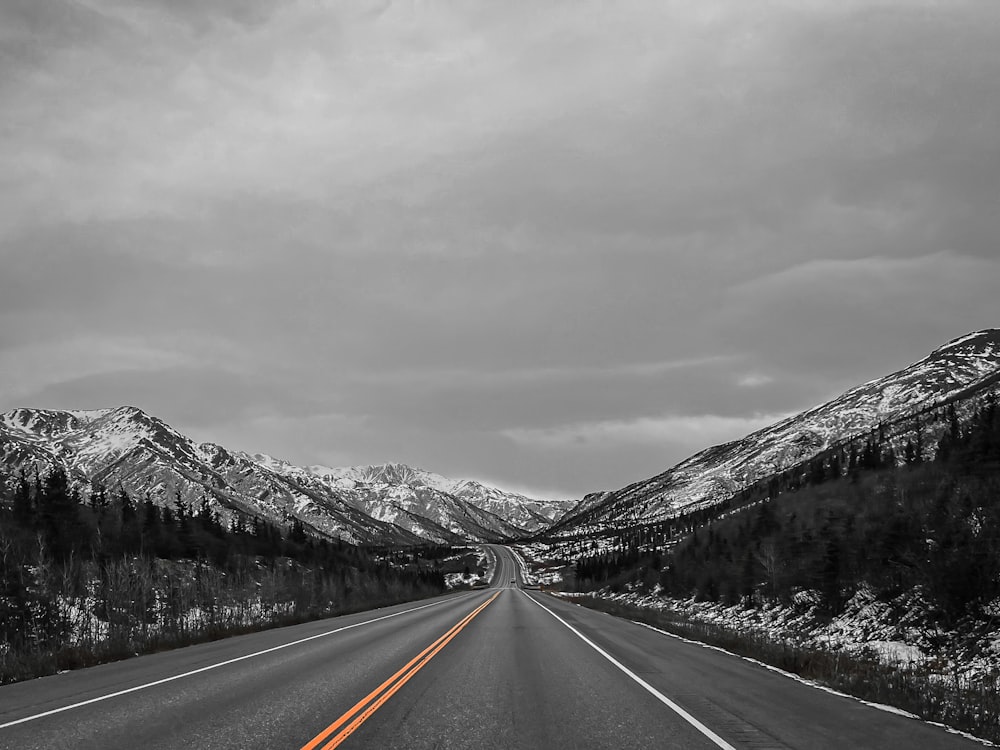 a black and white photo of a road with mountains in the background