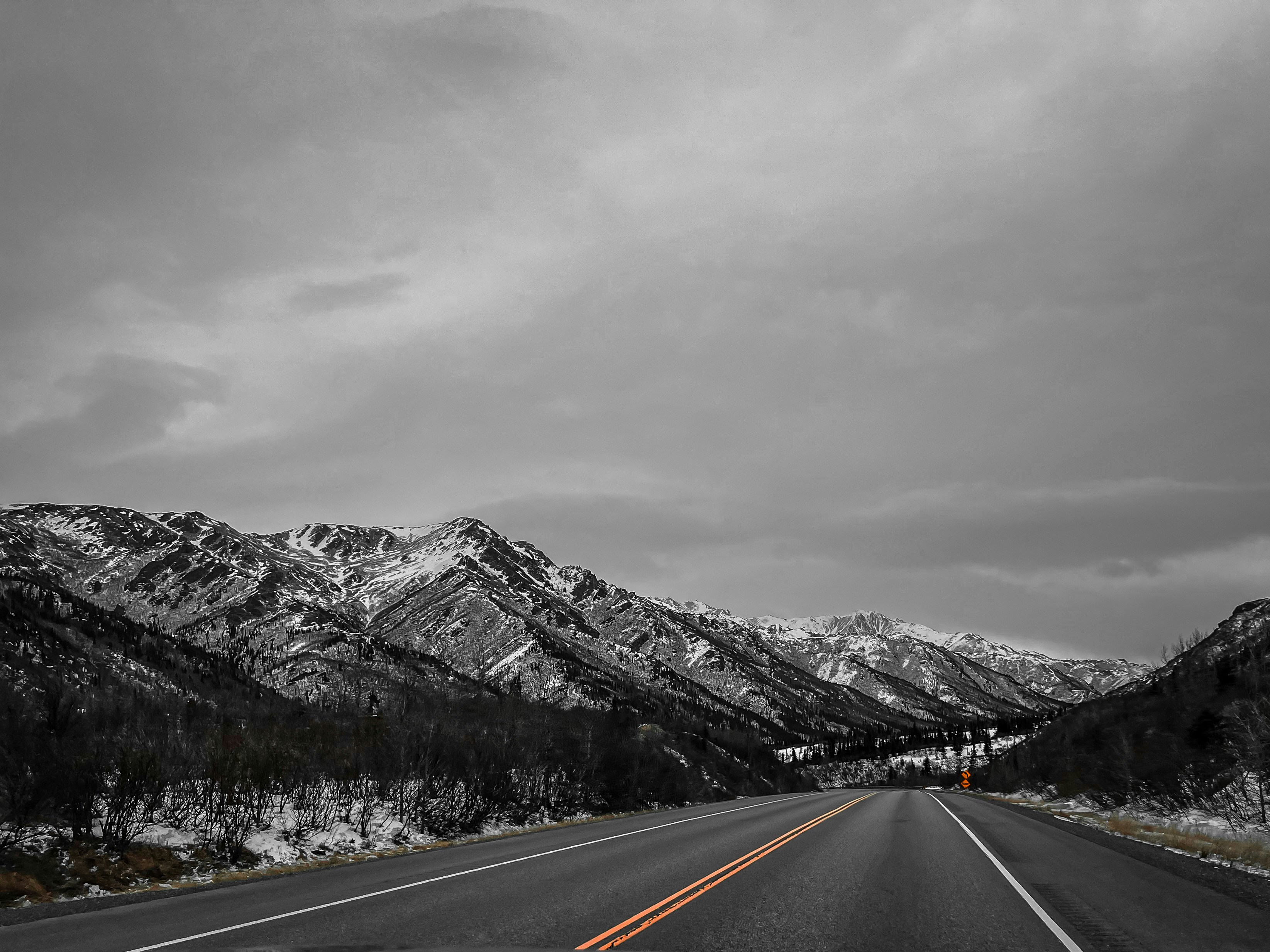 a black and white photo of a road with mountains in the background