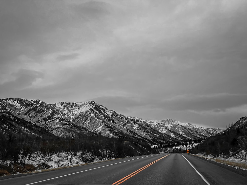 a black and white photo of a road with mountains in the background