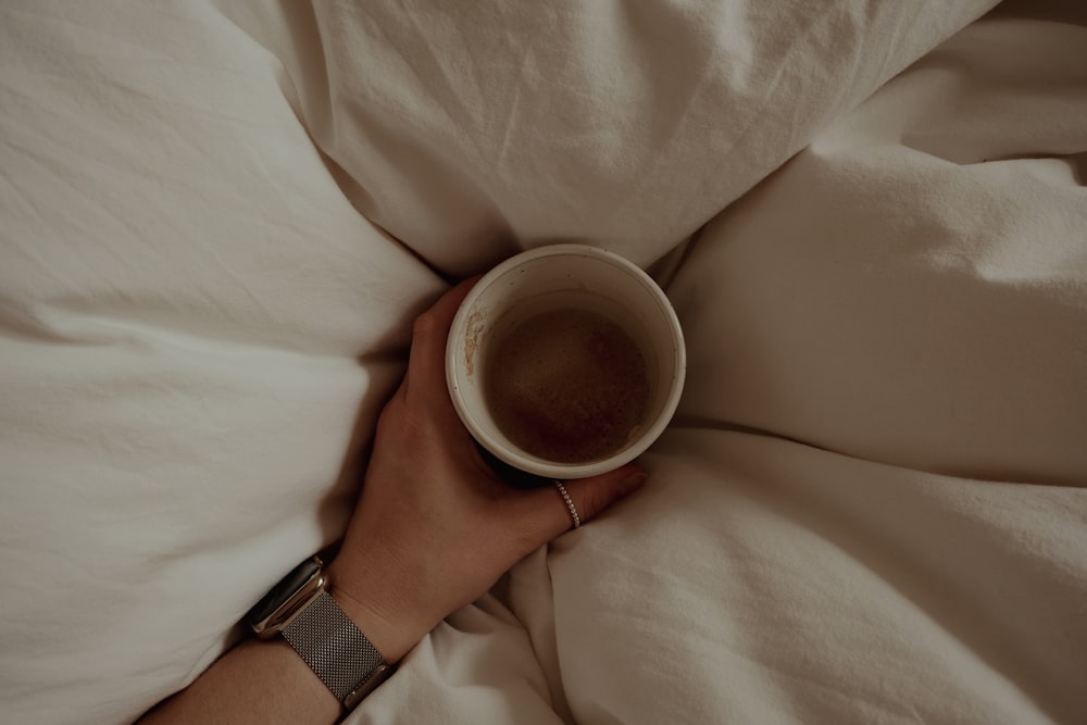 a person is holding a cup of coffee in bed
