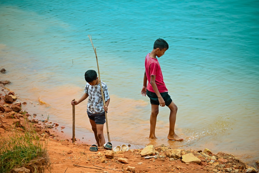 a couple of young boys standing next to a body of water